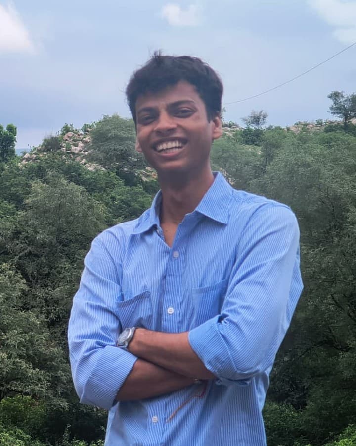 Aayush, who builds the tables, smiling outdoors in a blue shirt.